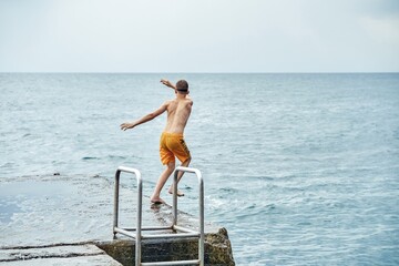 Fototapeta na wymiar Moments of schoolboy jumping from stone pier with ladder into sea doing tricks in combined image sequence