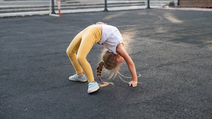 Caucasian girl doing bridge exercise on sports ground outdoors. 