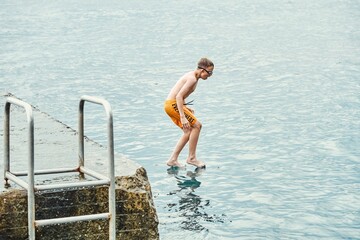 Schoolboy jumps from stone pier to sea. Moment of boy jumping and touching water. Guy looks like magician