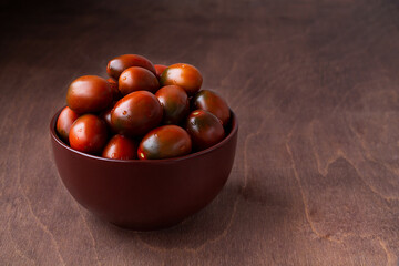 red tomatoes in a brown bowl. Fresh cherry tomatoes with water drops on wooden background. copy space