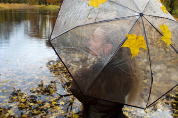 Woman under a transparent umbrella on a cloudy autumn day on the lake shore