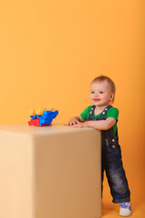 A little handsome boy plays with a toy on a light-colored pouffe . Studio shot of a baby boy against a yellow background.