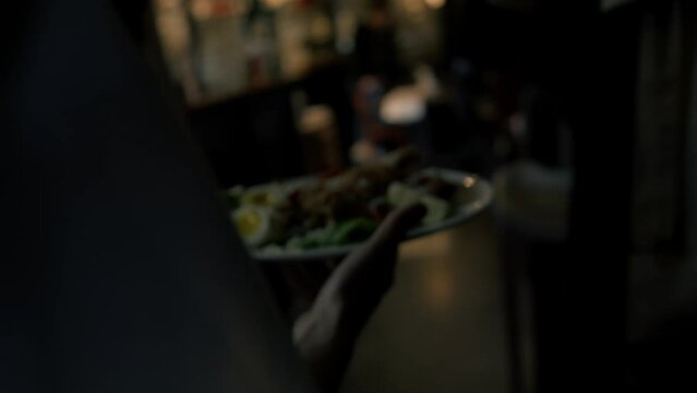Close-up - the waitress carries in her hand a Caesar salad with chicken to the guests, the interior of the restaurant