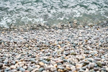 Crystal clean water washes pebbles lying on beach of sea. Wet pebbles lie near water edge waiting for rolling waves closeup