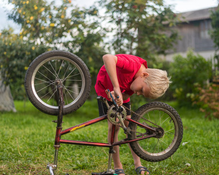 a boy in a red T-shirt repairs a bicycle - Powered by Adobe