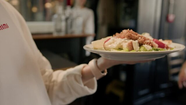 Close-up - the waitress carries in her hand a Caesar salad with chicken to the guests, the interior of the restaurant
