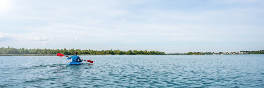 Panorama of a man in a blue kayak on a lake in summer