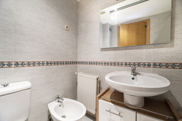 Bathroom with wooden cabinet under the white porcelain sink and frameless mirror on the wall with border
