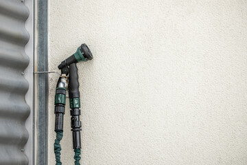 Water tap from a rubber green colored hose attached to the wall on a terrace with cream painted walls