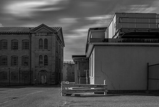 Daytime Exterior High Key Black And White Showing Limestone Prison Buildings With Barred Windows And An Empty Yard Under Dramatic Skies, Nobody