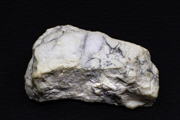 Close-up macro of a rough white howlite with light gray mineral veins, white buffalo stone, white turquoise crystal isolated on a black background surface
