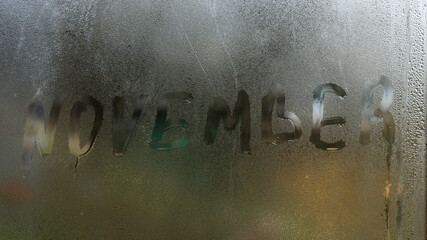 November inscription on the texture with condensation on the glass, a reaction to a sudden change...