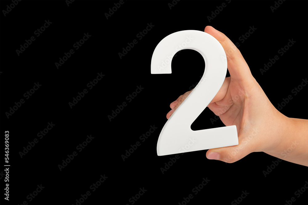 Fototapete number two in hand isolated on black background. number two white in a child's hand on a black backg