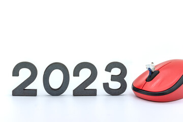 2023 Business New Year Concept. Closeup of businessman miniature figures sitting and reading a newspaper on computer mouse with number on white background.