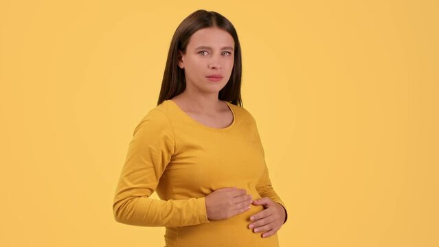 Pregnancy problems. Young unhappy pregnant woman looking at camera with teary eyes, caressing her belly
