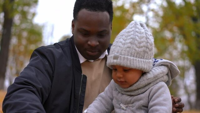Portrait of positive African American man and little boy playing with yellow leaves in autumn park smiling. Happy carefree father and son enjoying leisure together outdoors