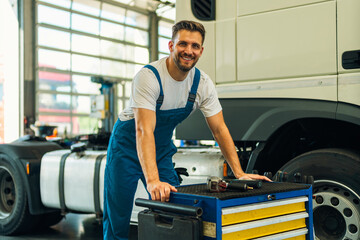 Portrait of positive smiling truck serviceman with tools standing by truck vehicle in workshop....