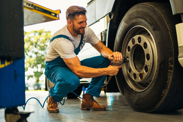 The mechanic squats next to the wheel of the truck and tightens the wheel screws. Use special...