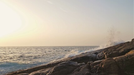 夕日に照らされる岩場に打ち付ける波しぶき