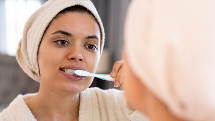 Oral hygiene, healthy teeth and care. Young woman brushing teeth with toothbrush and looking in mirror in bathroom interior 