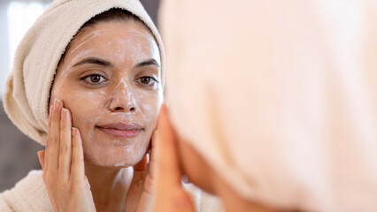 beauty, skin care and people concept - smiling young woman in skin care and looking to mirror at home bathroom