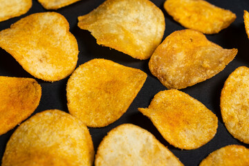 Delicious crispy potato chips with spices on a black background, top view