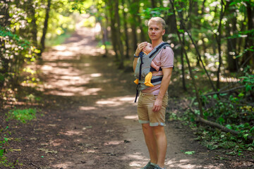 Fototapeta premium A young father walks with a baby in a sling backpack outside