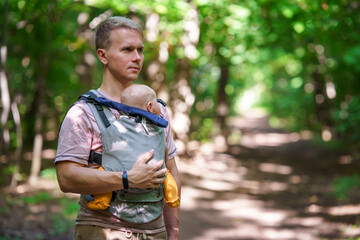 A young father walks with a baby in a sling backpack outside