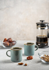 Healthy date seed coffee in two cups, coffee pot with dates fruits and seeds on grey concrete background
