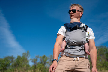 A young father walks with a baby in a sling backpack outside