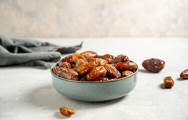 Dried date fruits in a grey bowl with grey napkin on concrete background. Close up. Copy space for text