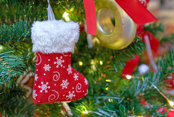 Red Christmas stocking for gifts on a Christmas tree with toys and garlands.