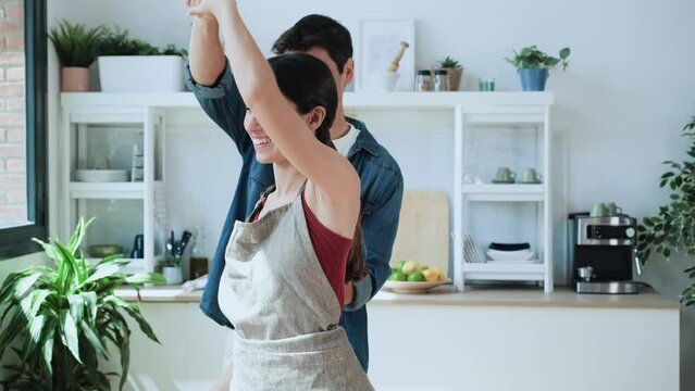 Video of lovely young couple cooking together dancing in the kitchen at home.
