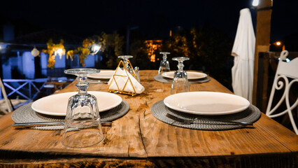 Empty table decorated with glasses, cutlery, dishes and placemats on the terrace on a summer evening. An empty decorated table ready to serve people.