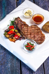 juicy fried steak with vegetables and sauce on a white plate on a blue wooden table