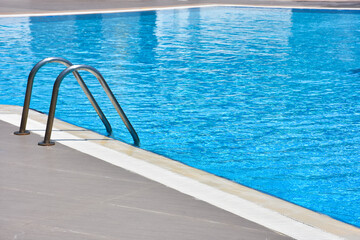 Close up shot of a blue color swimming pool with metal ladder. Modern swimming pool