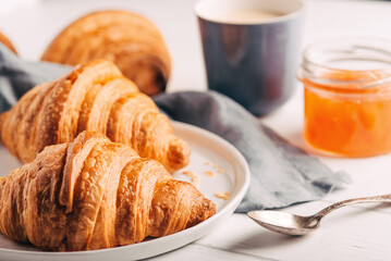 Plate with fresh croissants, jam and coffee on white wooden table. Close up.