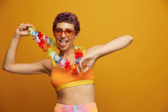 Woman with floral Hawaiian wreath around her neck has fun dancing and smiling in bright clothing against an orange background