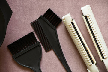 Black brushes for dyeing hair and a curling iron lie on a purple background, beauty salon, hairdresser's tools