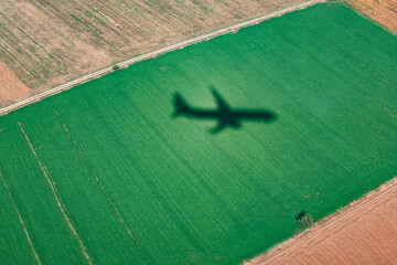 Silhouette of an aircraft reflected on the ground during a low altitude landing. Shadow of an airplane on a green field seen from the airplane window.