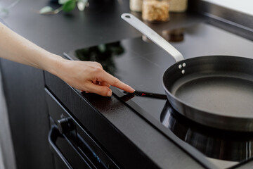 woman turn on induction stove at kitchen, cropped shot