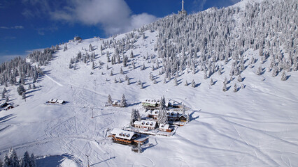 AERIAL: Snow-covered mountain chalets surrounded with snowy alpine ski resort