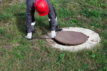 A male plumber opens a water well with a crowbar. Inspection and repair of water wells and septic tanks