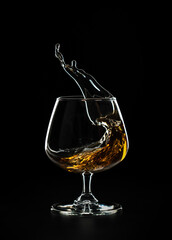 Fototapeta na wymiar A splash of cognac in a glass on a black background