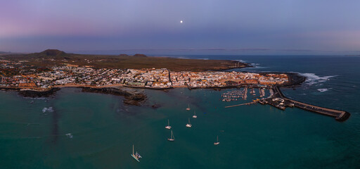 Mid level aerial panoramic view of Corralejo harbour, town and beaches early morning at moonset, Fuerteventura