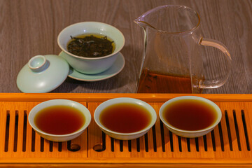 Brewing Chinese tea in a ceramic gaiwan during a tea ceremony close-up. Gaiwan and other tea accessories for the ceremony on a bamboo tea board.