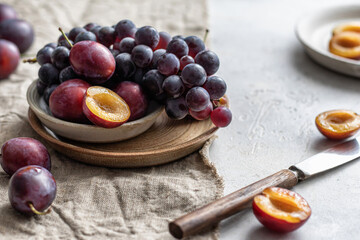 Ripe grapes and plums on linen tablecloth with knife, selective focus. Autumn mood still life composition