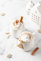 Two mugs of hot chocolate or cocoa with whipped cream and cinnamon on white marble background close up. Xmas mock up, festive card. Traditional Christmas drinks