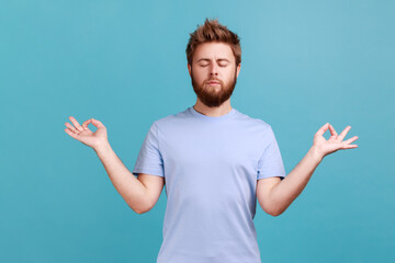 Portrait of calm man standing with raised arms and doing yoga meditating exercise, keeping eyes...