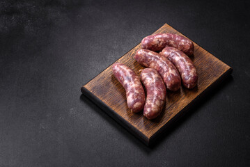 Raw pork sausages grill with spices and herbs on a dark concrete table